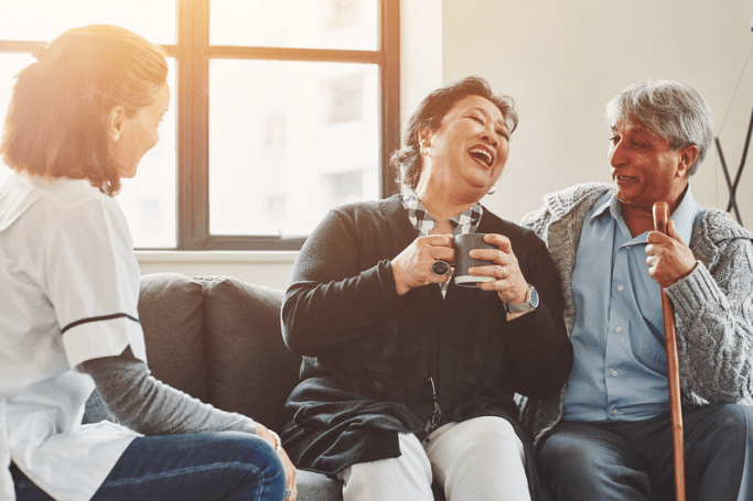 OT carering for 2 elderly people, man and woman talking and laughing over tea