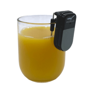 Uccello Liquid Level Indicator sitting on the rim of a glass of orange Juice