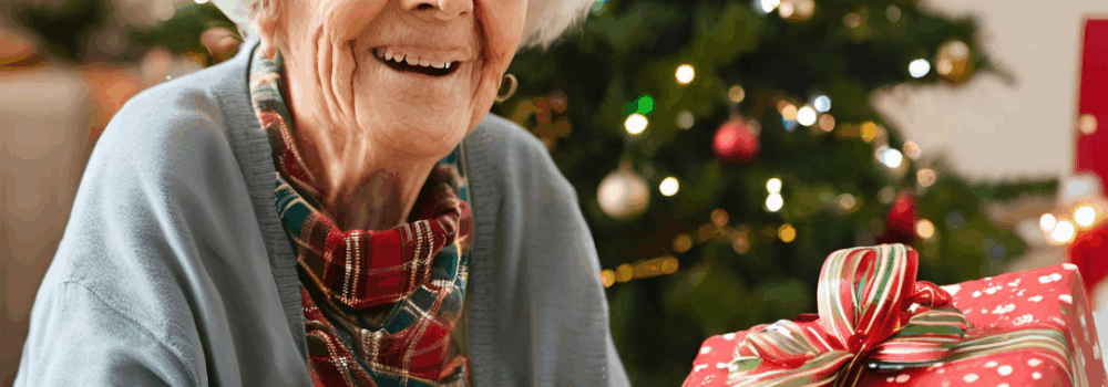 Elderly woman sitting by the Christmas tree with a wrapped present