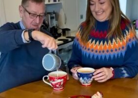 Elderly father and daughter enjoying a cup of tea together with festive Christmas jumpers on