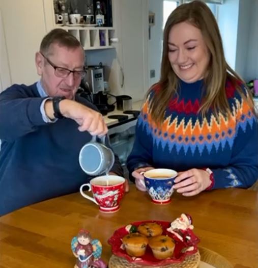 Elderly father and daughter enjoying a cup of tea together with festive Christmas jumpers on